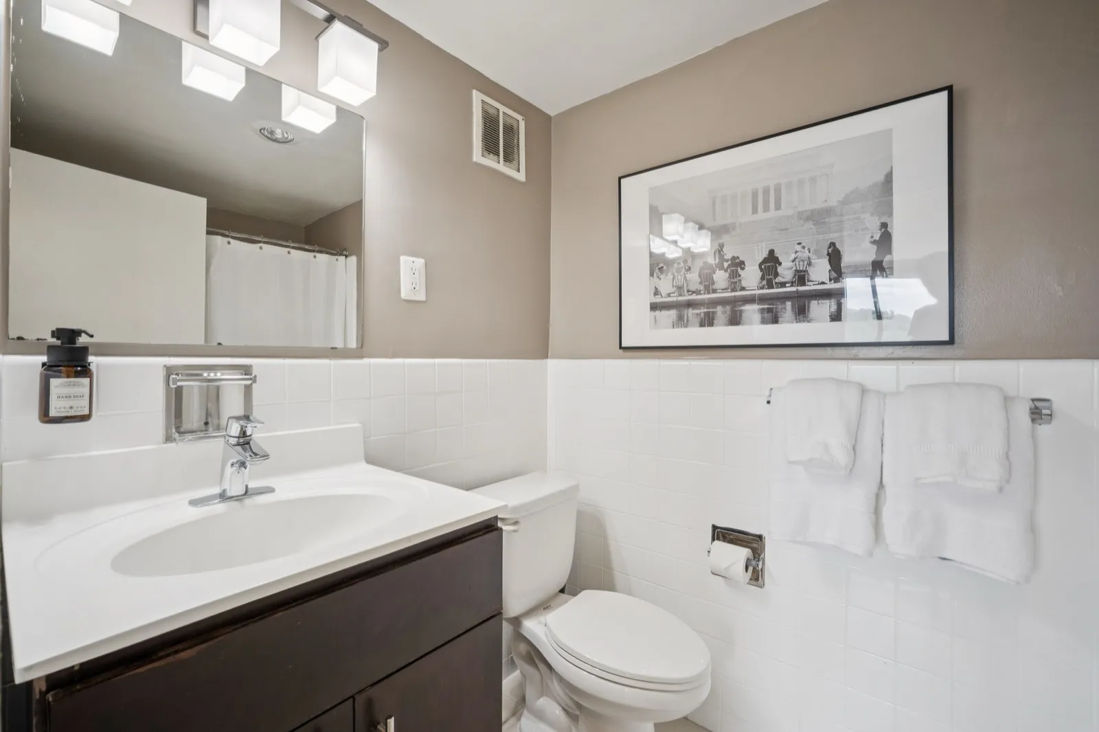 Modern bathroom with a dark vanity, chrome fixtures, and framed artwork in a Crystal City furnished apartment