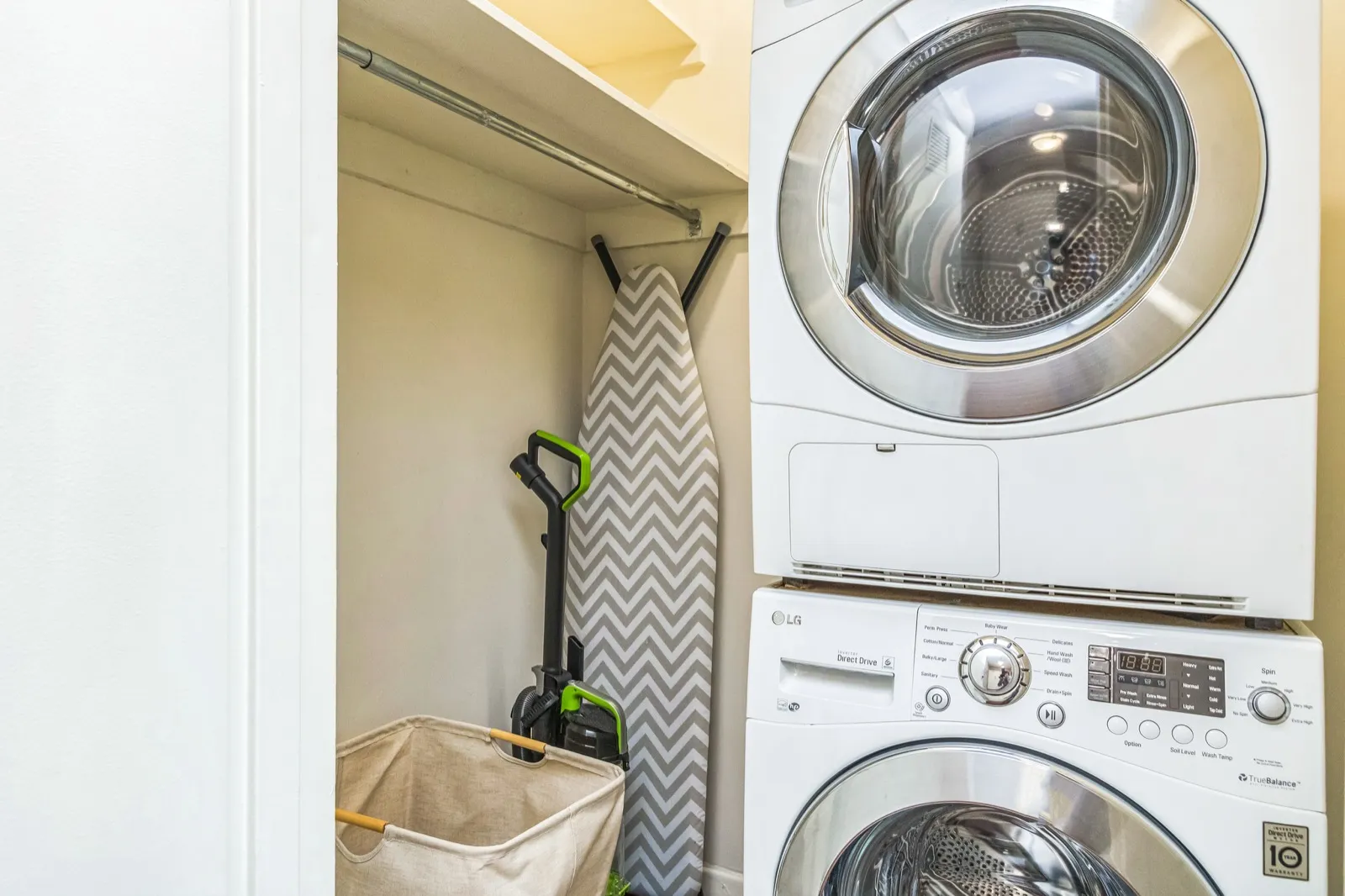 In-unit stacked LG washer and dryer with ironing board and vacuum in an Arlington VA furnished apartment
