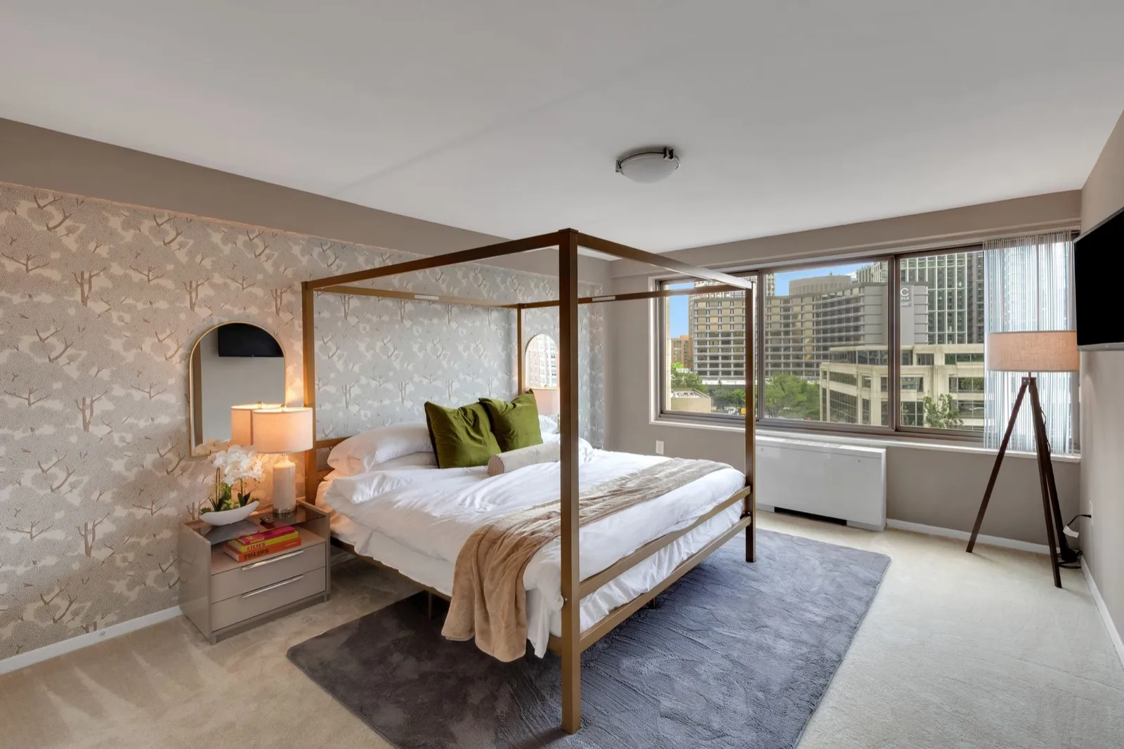 Primary bedroom with a gold canopy king bed, botanical wallpaper, and a city skyline window in National Landing